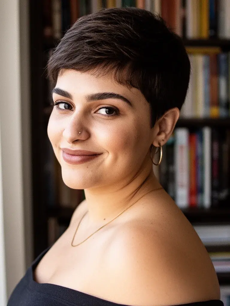 Boy cut three-quarter view on a Brazilian woman with dark brown hair, bookshelf background